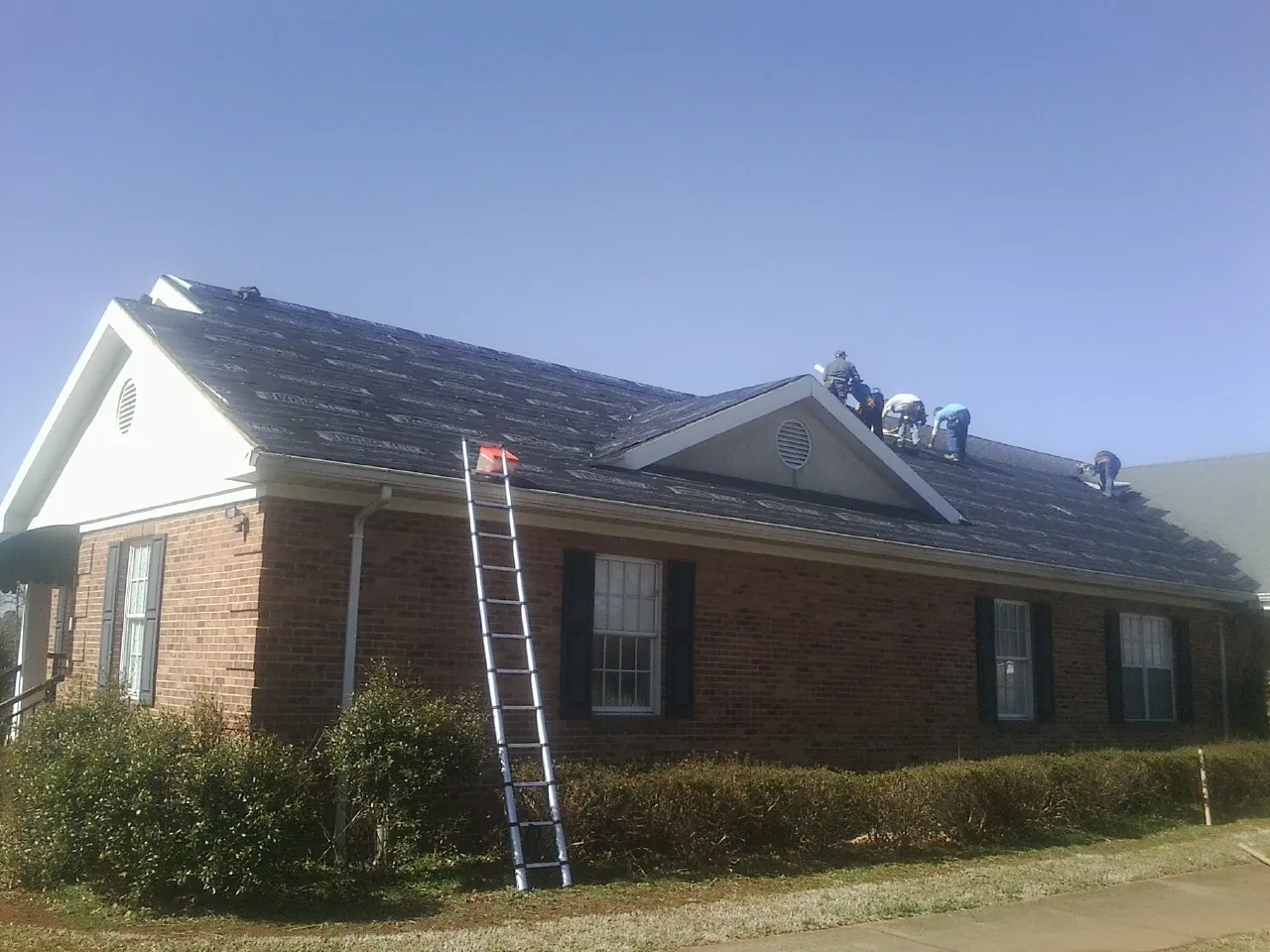 Crew tearing shingles off a brick ranch roof with a ladder set — Emergency Roof Repair work by our crew in Columbia