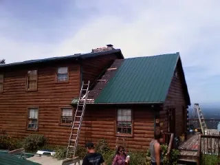 Green metal roof going on a two story log home with ladders set in Columbia